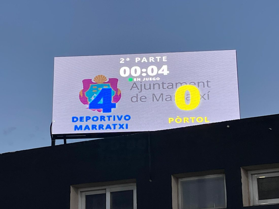 Una pantalla LED en lo alto de un edificio del campo mostrando el marcador de un partido, 4 a 0, en la segunda parte